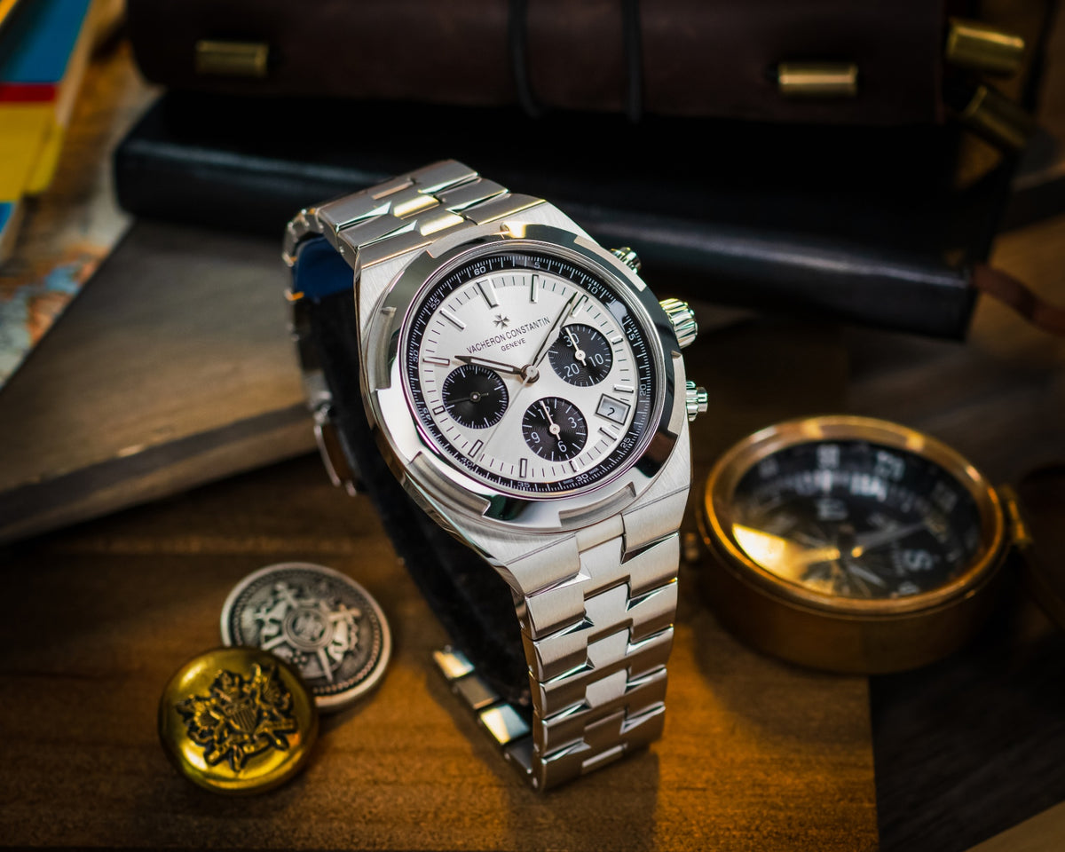 Vacheron Constantin Overseas chronograph in stainless steel displayed with vintage compass and collectible medallions